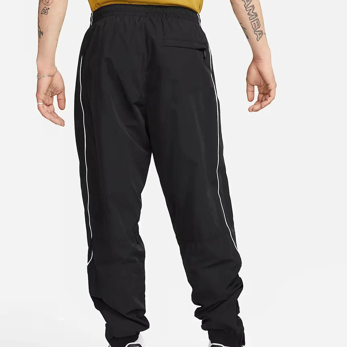 Nike Solo Swoosh Men’s Track Pants in black, back view. Shows secure zip pocket, reflective piping along legs, adjustable cuffs and lightweight nylon fabric.